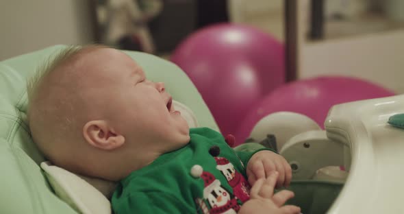 Toddler in Chair Crying and Mother Entertaining Him with Toy alt