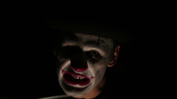Terrible Man in the Makeup of a Clown Looks at the Camera, Laughs and Licks a Knife Blade. Terrible