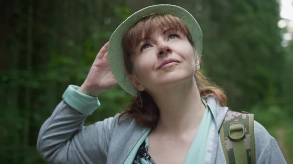Happy Brunette Woman with Hat in the Forest Looks Around Travel Concept