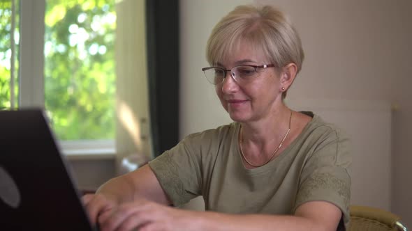 Smiling Elderly Women with Poor Eyesight in the Glasses is Typing on the Laptop