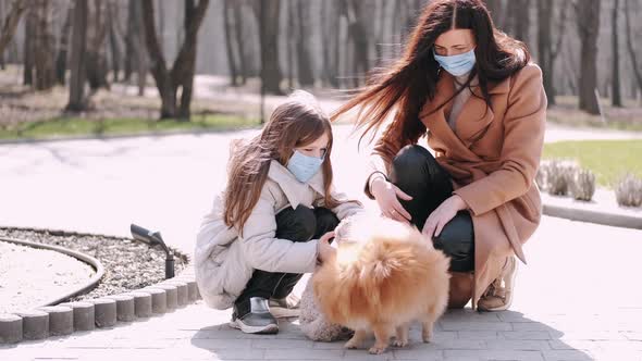 European Mother and Her Daughter Are Walking with a Dog During Quarantine in the Spring Park alt