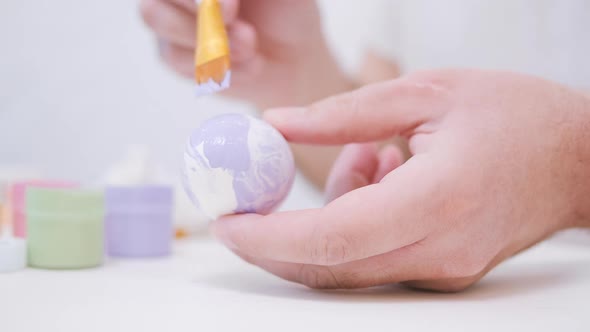 Men's Hands are Painting an Easter Egg with a Brush alt