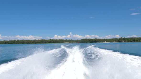 Trails of a speed boat with tropical island in the background. alt