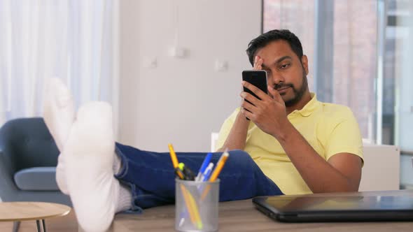Indian Man with Smartphone Resting Feet on Table alt