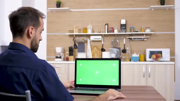 Man at the Table in the Kitchen Looking at Laptop alt