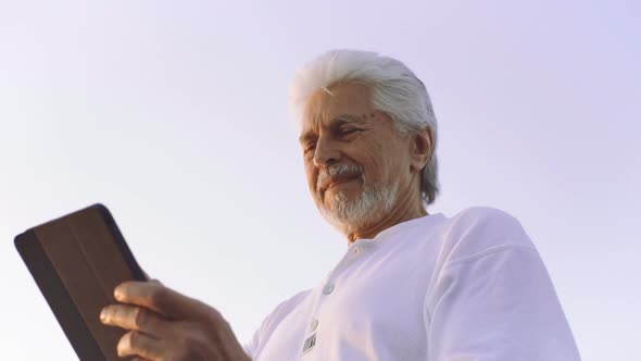 Portrait of Retirement Handsome Senior Man Using Tablet Computer on Seafront and Smiling alt