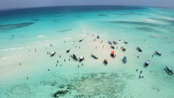 People walking in shallow tropical ocean waters between anchored boats. Zanzibar alt