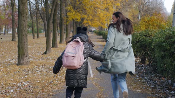 Mom and Little Daughter are Running Through the Autumn Park to School