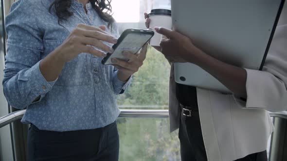Female Business Agents with Gadgets and Coffee To Go in Elevator alt