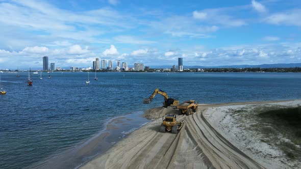 Heavy machinery working on a coastal rejuvenation project with a city skyline in the distance. Panor alt