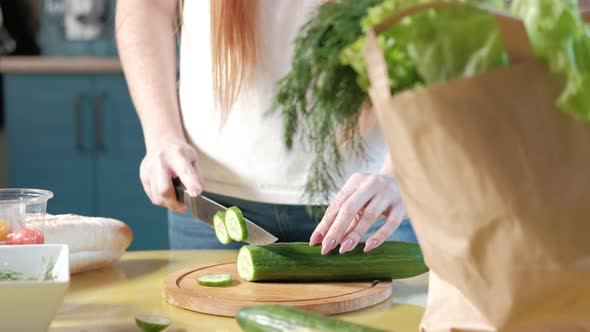 woman in the kitchen on the table cuts ripe cucumbers for a vegetable salad alt