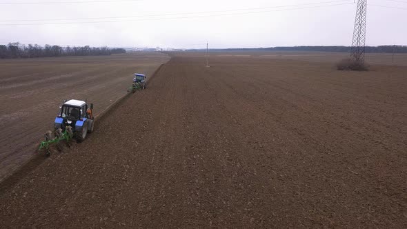 Flying Behind Two Tractors Plowing a Field in Cloudy Weather