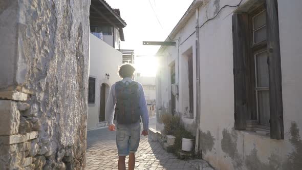 The Camera Follows a Man with a Backpack Walking in the Old City of Greece