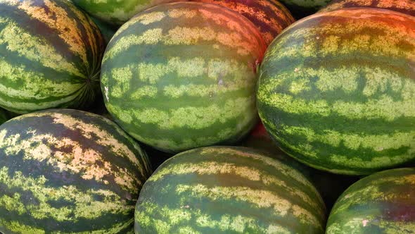 Large ripe watermelons and half a watermelon lie under a red awning in the market.