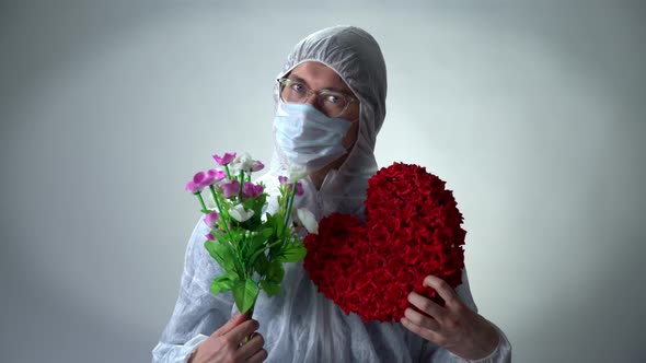 A Man in a Protective Suit, Medical Mask and Glasses Shows a Heart of Roses and Flowers on a White
