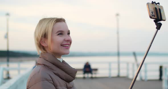Happy Female Blogger Records a Video While Standing on a Pier alt