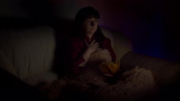 Sad Brunette Woman Sits in Sofa with Chips at Night and Watches Tv with Emotion alt