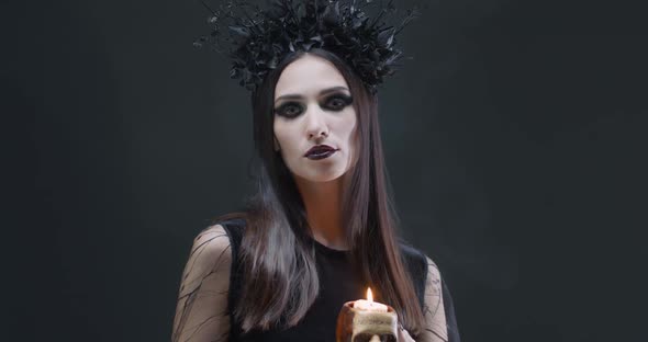 Mystical Female in Black Attire Holds a Skull with a Burning Candle and Looking at the Camera, the alt