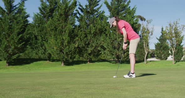 Caucasian female golf player taking shot from bunker standing on golf field alt