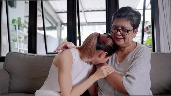 elderly mother comforts her weeping daughter on her shoulder.