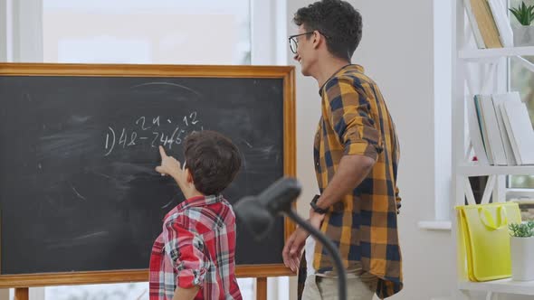 Young Smiling Middle Eastern Teacher in Eyeglasses Listening to Pupil Explaining Math Problem alt