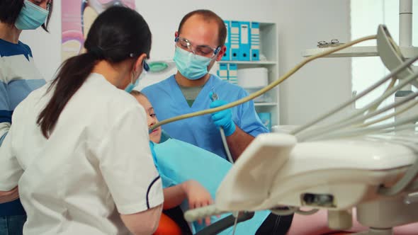 Stomatologist with Mask and Gloves Using Drill Tool for Cleaning Teeth of Kid alt
