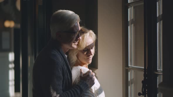 Mature Smiling Couple Looking Out Through Window Indoors alt