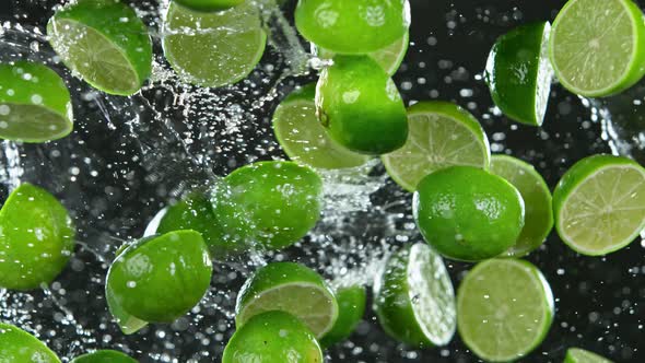 Super Slow Motion Shot of Flying Fresh Limes and Water Side Splash Isolated on Black at 1000 Fps alt