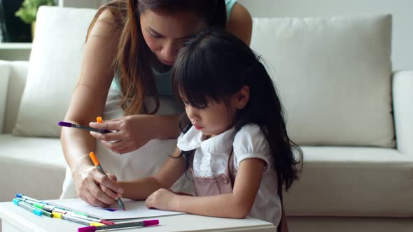 Young mother teaching her daughter painting colour pencil on paper 