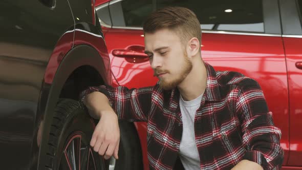 Young Man Examining Wheels and Tires of a New Car at the Dealership alt