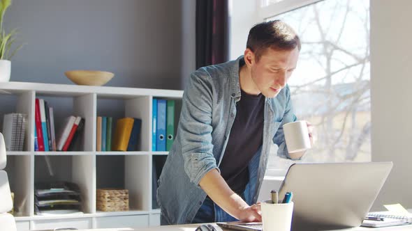 Young male entrepreneur works at home office at the computer. alt