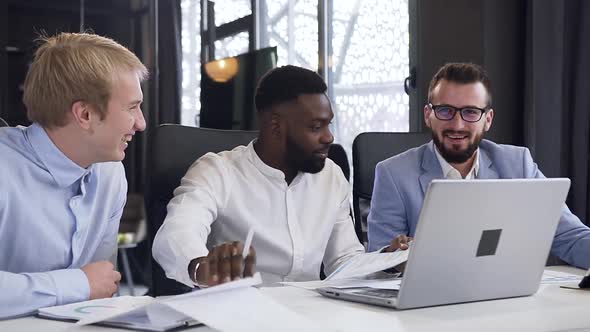 Multiracial Male Colleagues Working Together with Financial Documents Under Their Joint Project alt