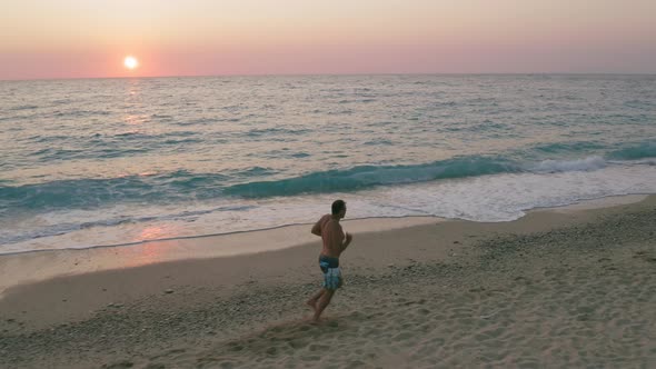 Aerial Low Altitude Side Follow View of Man Running Along the Beach in Sunset Golden Sunlight