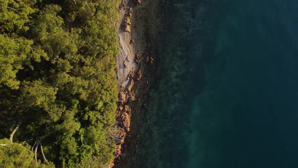 High revealing view of a rugged coastal headland next to tropical blue swimming area. Drone view loo alt
