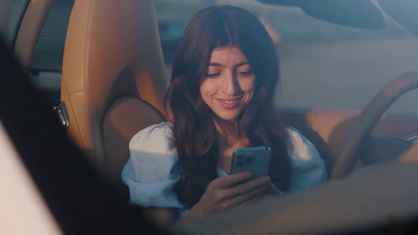 Beautiful Stylish Woman Sits in Her Luxury White Convertible and Uses Smartphone for Chatting alt