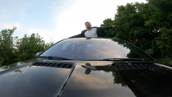 Happy Funny Man Standing Out of Car Sunroof and Showing Joyful or Crazy Emotions alt