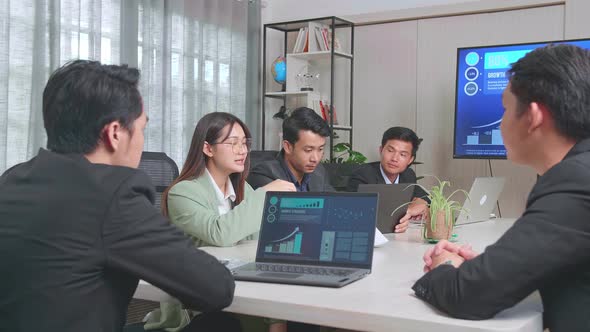Asian Team Have Meeting In A Conference Room. They Share Opinions, Statistics Show On Laptop And Tv alt