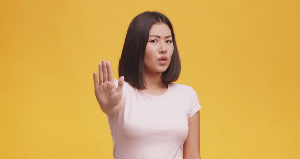 Displeased Young Asian Woman Saying No, Showing Stop Gesture with Palm, Orange Studio Background alt