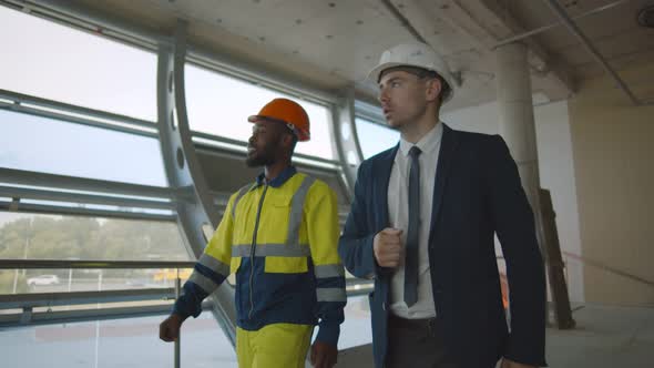 Young Engineer Discussing with Building Worker on Construction Site alt