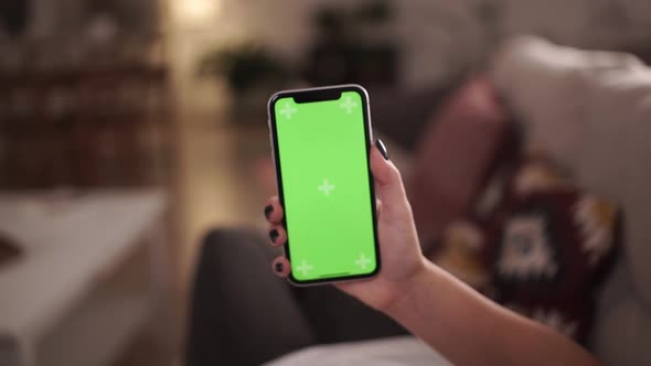 Home Isolated. Back View of Woman Holding Chroma Key Green Screen Smartphone Watching Content