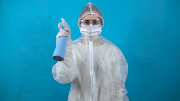 Young Woman in a Protective Suit Dispenser in Hand. A Girl Sprinkles an Antiseptic on a Blue alt