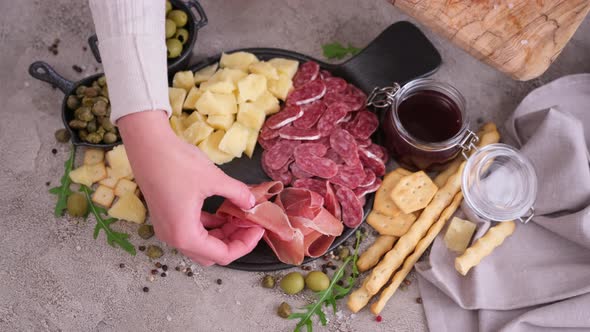 Making Meat and Cheese Antipasto Plater Woman Putting Pieces of Prosciutto Ham on Stone Serving alt