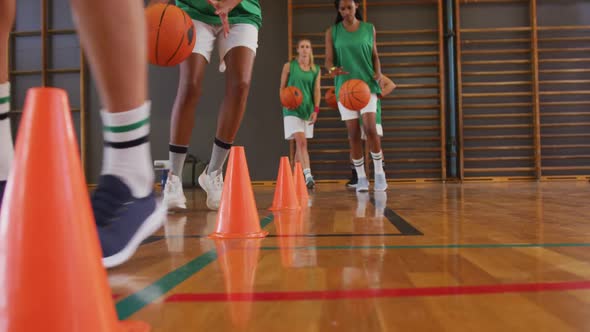 Mid section of diverse female basketball team and coach practice dribbling ball alt