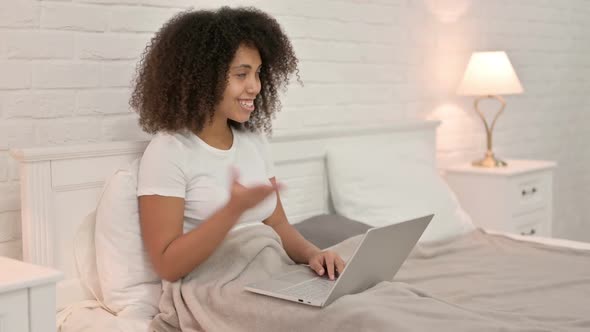 Video Chat on Laptop By Young African Woman in Bed alt