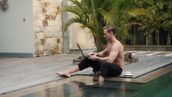 Sporty Caucasian Topless Man Works on Vacation Outdoor at the Pool with Laptop alt