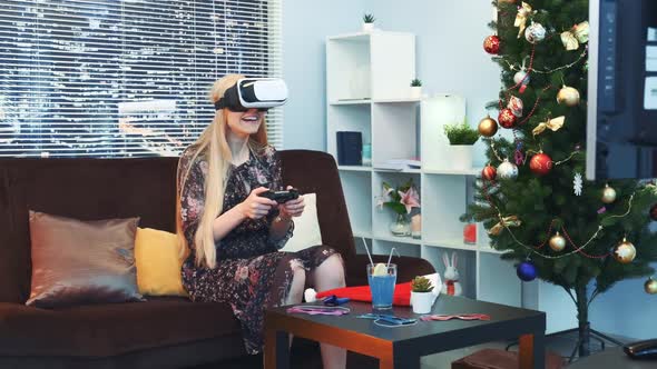 Joyful Woman Playing a Game with Joystick in Virtual Reality Glasses in Front of TV on Christmas alt