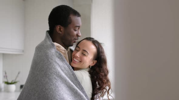 Loving Young Couple Cuddling At Home In Kitchen Wrapped In Cosy Blanket