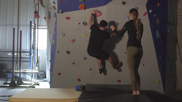 Couple in gym working out on rock climbing wall alt