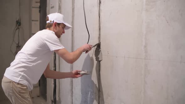 A worker closes a channel with a cement mortar with a cable in the wall alt