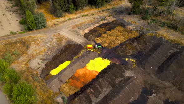 Aerial orbit of a tractor discarding orange shells on a compost area in a farm field surrounded by t alt